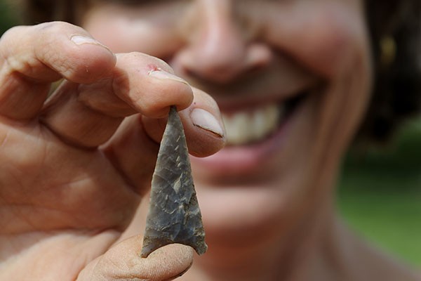 Smiling archaeologist holding a flint arrowhead.